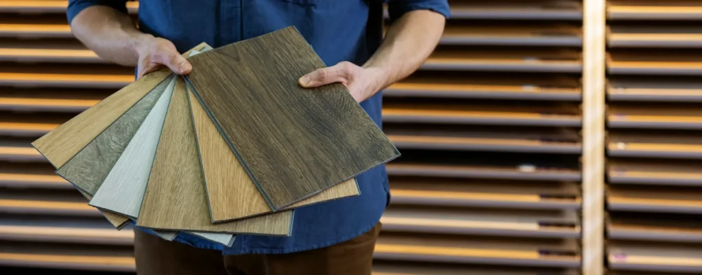A flooring specialist holding a selection of wood-look vinyl flooring samples in various tones and grain patterns at a showroom - FloorXpert