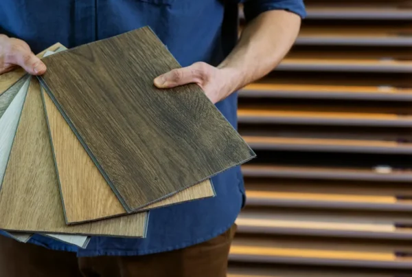 A flooring specialist holding a selection of wood-look vinyl flooring samples in various tones and grain patterns at a showroom - FloorXpert