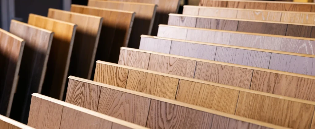 Rows of laminate flooring samples in a showroom display, ranging from warm honey oak and walnut tones to cool grey and ash finishes - FloorXpert