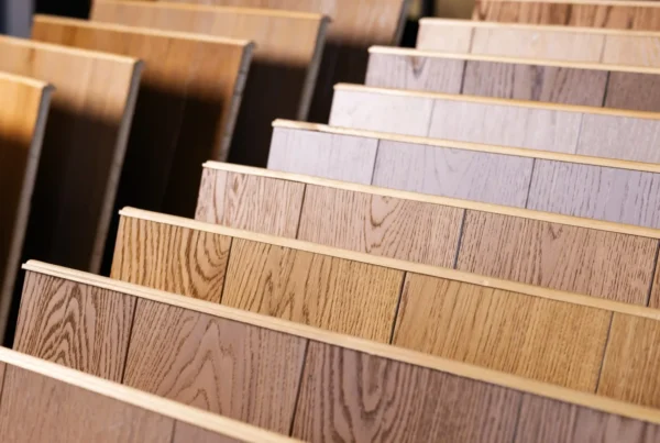 Rows of laminate flooring samples in a showroom display, ranging from warm honey oak and walnut tones to cool grey and ash finishes - FloorXpert